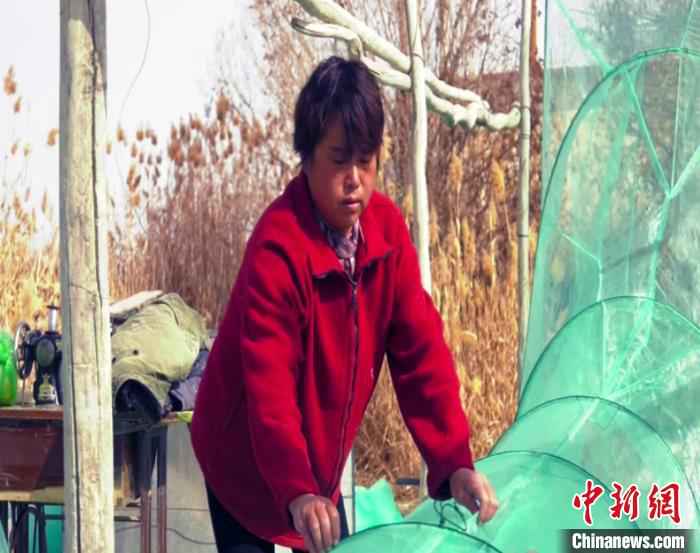 渔民李英查看刚刚织好的新网。 都古尔加甫 摄  “促民增收打更多的鱼”中国最大内陆淡水湖博斯腾湖进入禁渔期